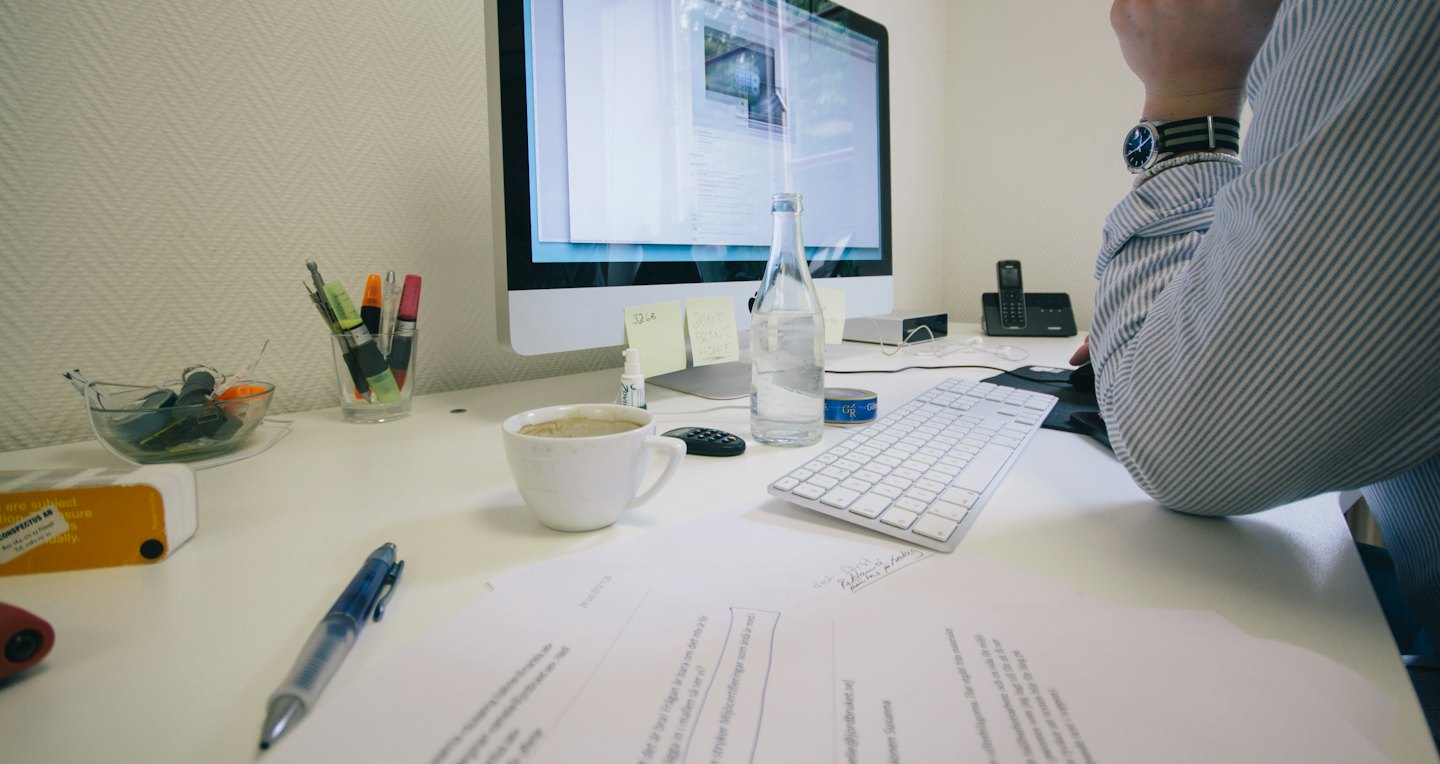 Person working at a desk with computer and documents.